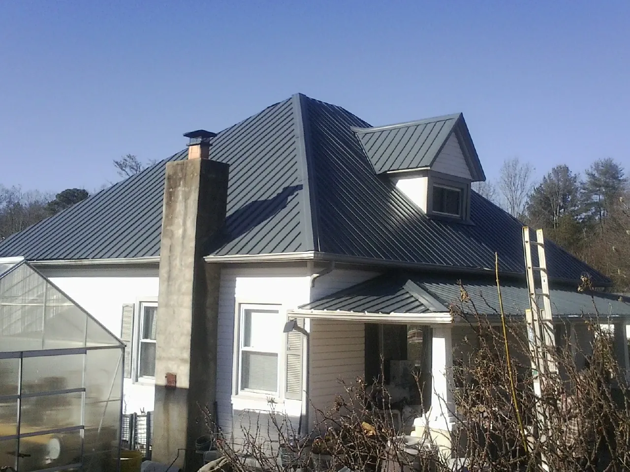 Dark blue standing seam metal roof on a white farmhouse with dormer — Slate & Tile Roof Repair by Roofing Brothers in Pollock