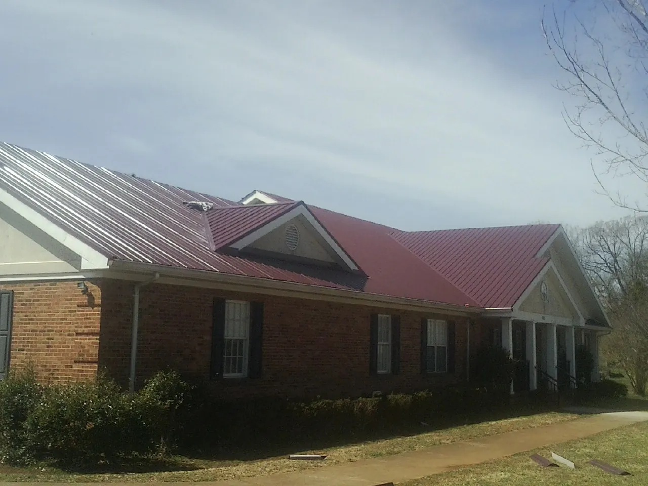 Red metal roof with gabled entries on a long brick building, from a Hail Damage Roof Repair job in Pollock